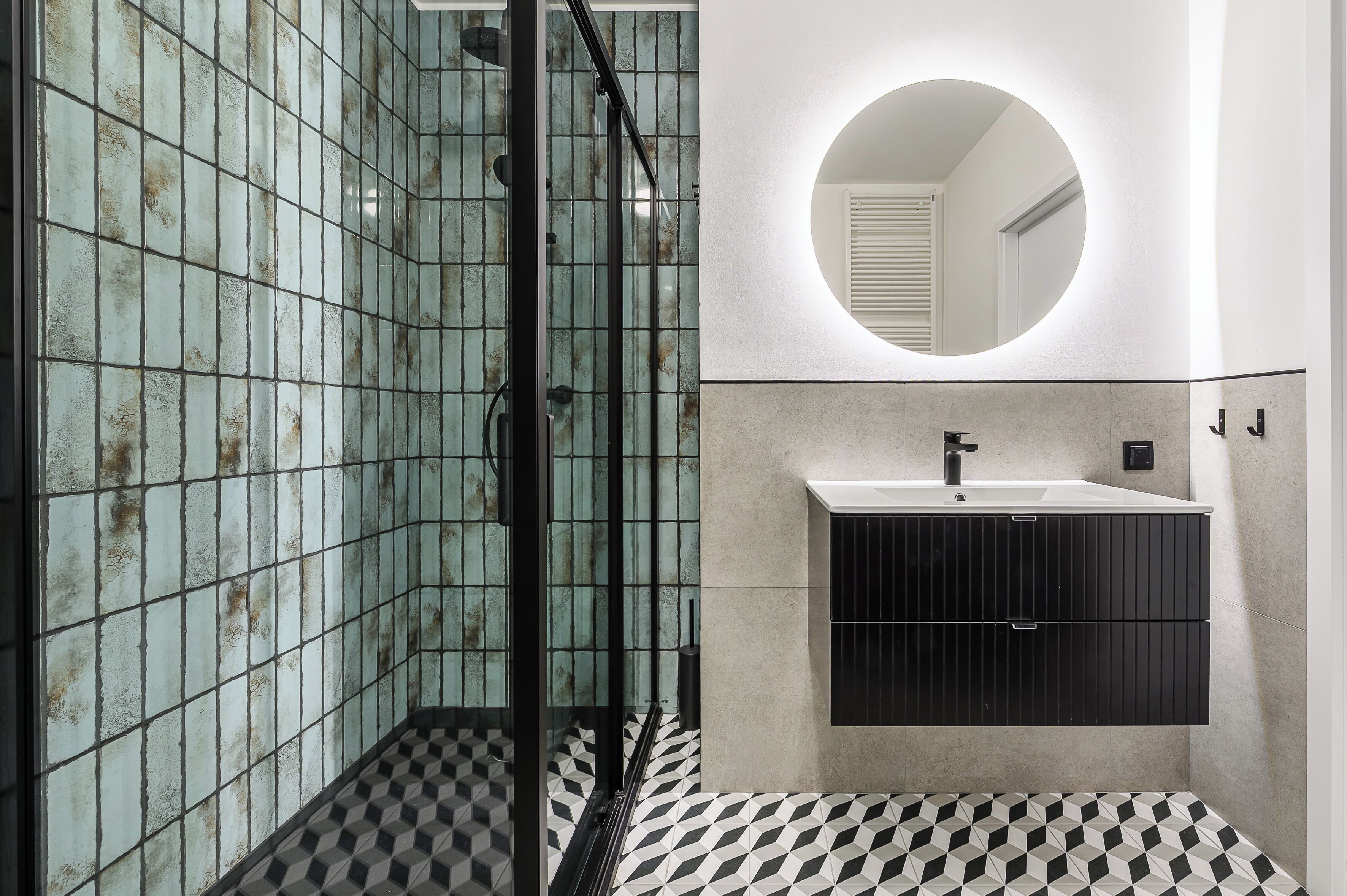 A bathroom with a glass shower enclosure, a round mirror, a sink with a black cabinet, and a checkered floor.