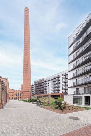Ein hoher Backsteinschornstein, moderne Wohngebäude und ein gepflasterter Weg.