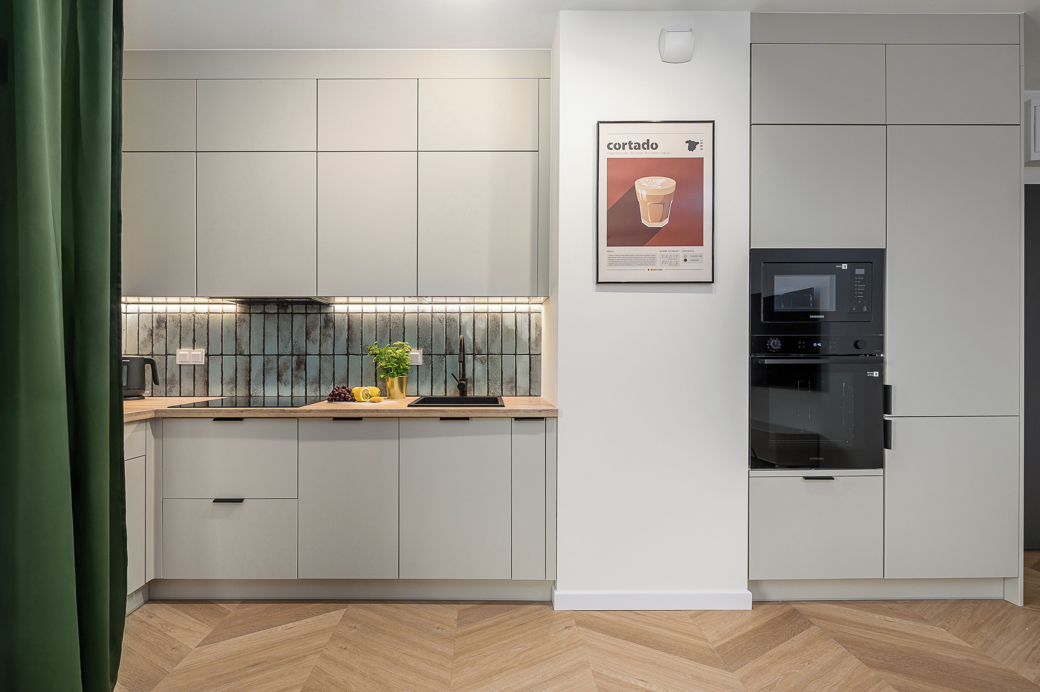 Een moderne keuken met inbouwapparatuur, een visgraat houten vloer en een ingelijst poster aan de muur.