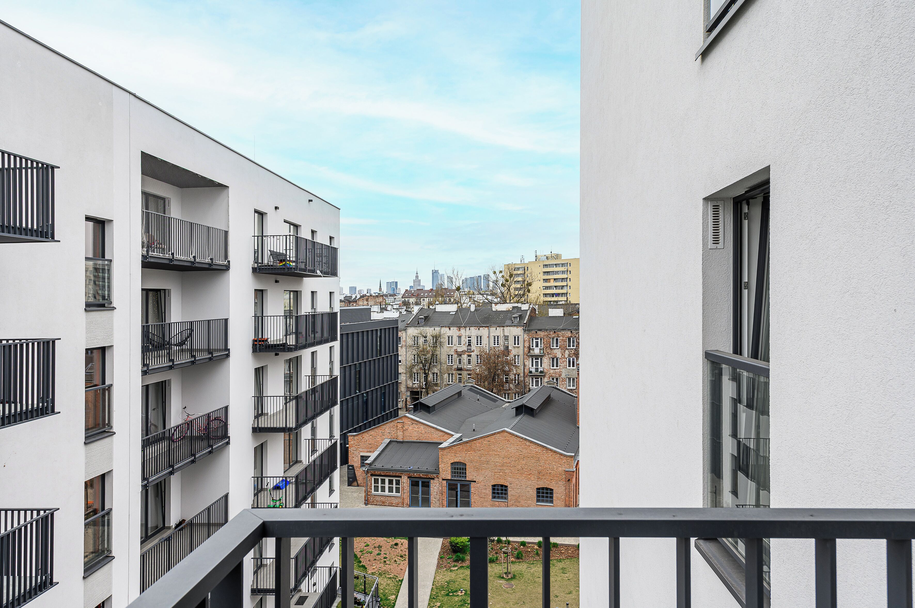 A multi-story building with balconies, a brick building in the background, and a clear sky.