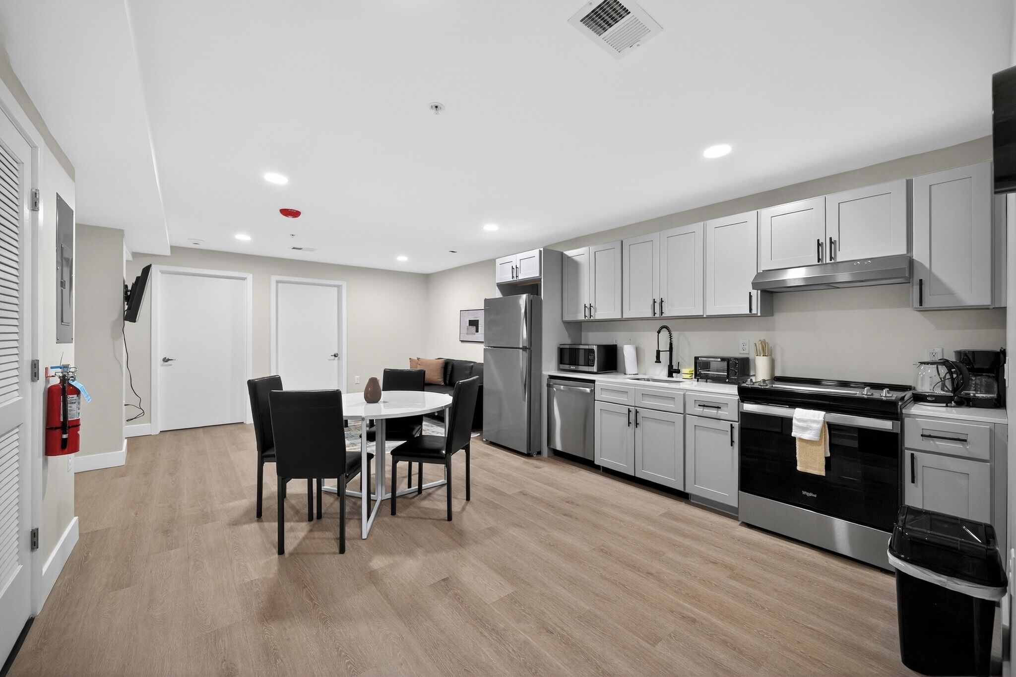 A modern kitchen with grey cabinets, stainless steel appliances, and a dining area with a table and chairs.
