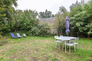 An outdoor seating area with a table and chairs, surrounded by greenery and a stone wall.