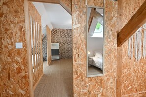 A room with a sloped ceiling, wooden walls, a bed, a nightstand, and a mirror.