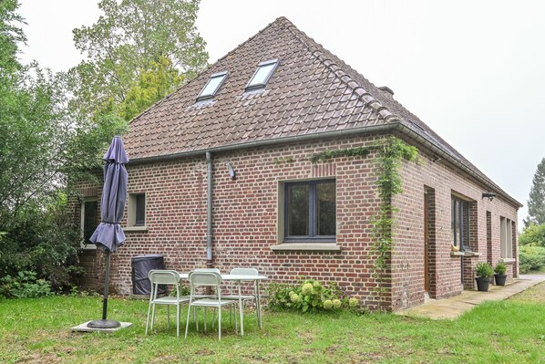 A brick house with a tiled roof, a covered outdoor seating area, and a garden.
