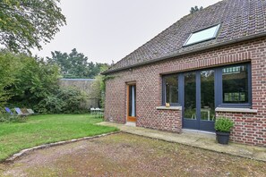 A brick house with a large window, a door, and a small garden area with grass and a gravel path.