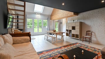 Ein modernes Wohnzimmer mit einer Couch, einem Esstisch mit Bänken, einem Couchtisch und einem Bücherregal.