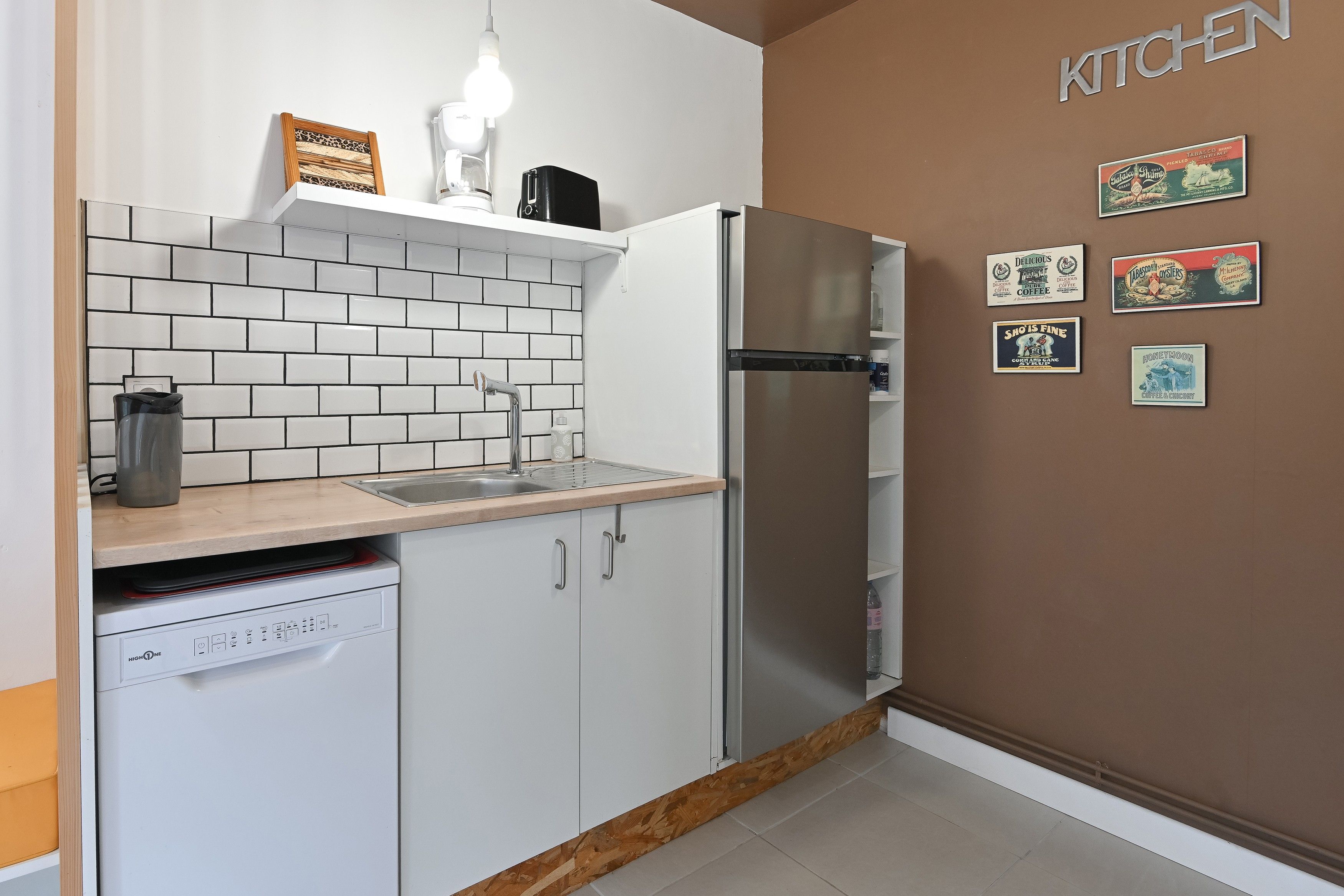 Eine kleine Küche mit weißen Schränken, einem Edelstahlkühlschrank und einer gefliesten Spritzschutzwand.
