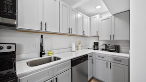 A modern kitchen with white cabinets, a dishwasher, a stove, and a coffee maker. - Contemporary 2BR near dining and transit (Reading)