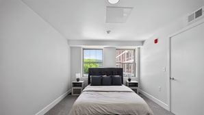 A bedroom with a bed, two bedside tables, a window with a view, a door, and a ceiling light. - Contemporary 2BR near dining and transit (Reading)