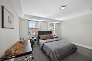 Ein modernes Schlafzimmer mit einem Bett, einem Schreibtisch und einem Fenster mit Blick auf die Stadt.