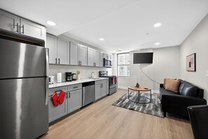 Eine moderne Küche mit Edelstahlgeräten, grauen Schränken und einem flachbildfernseher an der Wand.