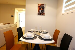 Ein Essbereich mit einem runden Tisch, gedeckt für vier Personen, umgeben von Stühlen, mit einer weißen Wand und einer Tür im Hintergrund.