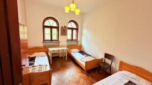 A room with two wooden beds, a small table, a chair, and two windows with curtains.