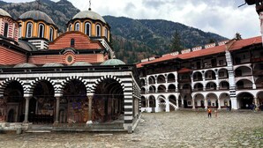 A historic building with arches and domes, a courtyard, and a mountainous backdrop.