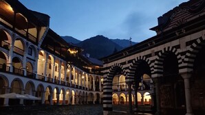 A courtyard with stone paving, white and black striped arches, and a building with multiple balconies. - Exclusive Stay Inside the Rila Monastery (Rila)