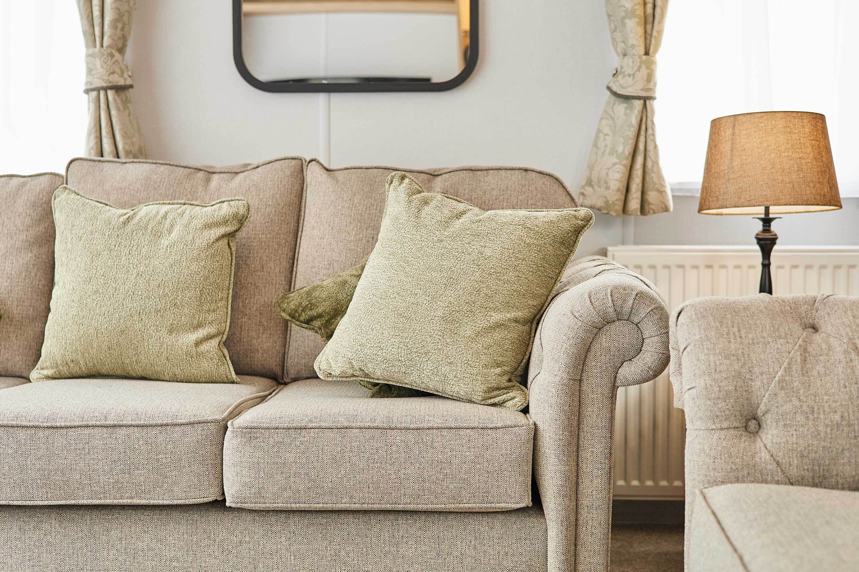 A beige sofa with two pillows, a lamp, and curtains in a room.