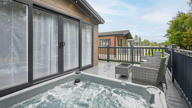 Ein Whirlpool auf einer Holzterrasse mit Blick auf andere Gebäude und ein eingezäuntes Grundstück.