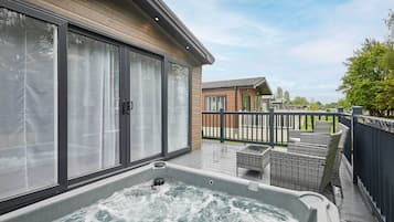 Un bain à remous sur une terrasse en bois, avec vue sur d’autres bâtiments et une zone délimitée par une clôture.
