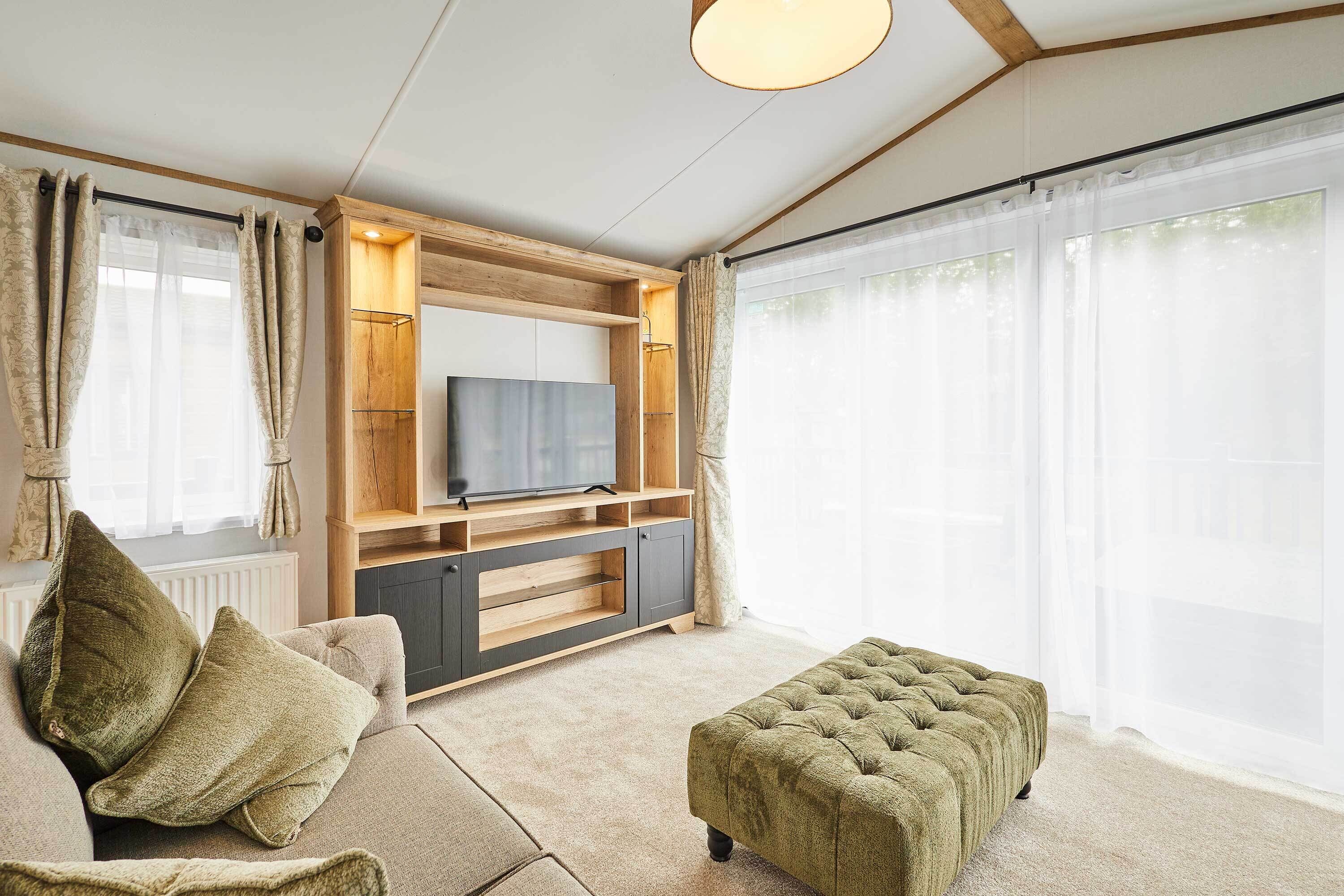 Un salon comprenant un canapé, un pouf, un téléviseur, un meuble de rangement en bois et de grandes fenêtres.