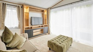 Ein Wohnzimmer mit einer Couch, einem Hocker, einem Fernseher, einer Holz-Unterhaltungseinheit und großen Fenstern.