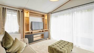Un salon comprenant un canapé, un pouf, un téléviseur, un meuble de rangement en bois et de grandes fenêtres.