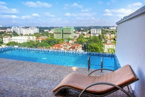 Ein Pool mit Blick auf umliegende Gebäude, eine Liege und ein gefliester Boden.