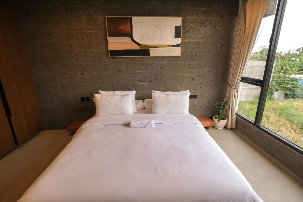 A bedroom with a bed, a potted plant, and a window with curtains.
