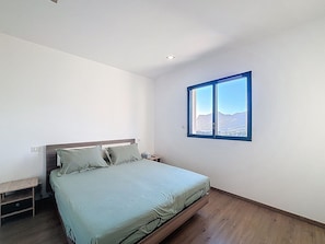 Un dormitorio con cama, mesita de noche, ventana y vistas a montañas, además de suelo de madera.