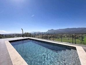 Una piscina rectangular con agua cristalina, rodeada por una solería y una barandilla de metal.