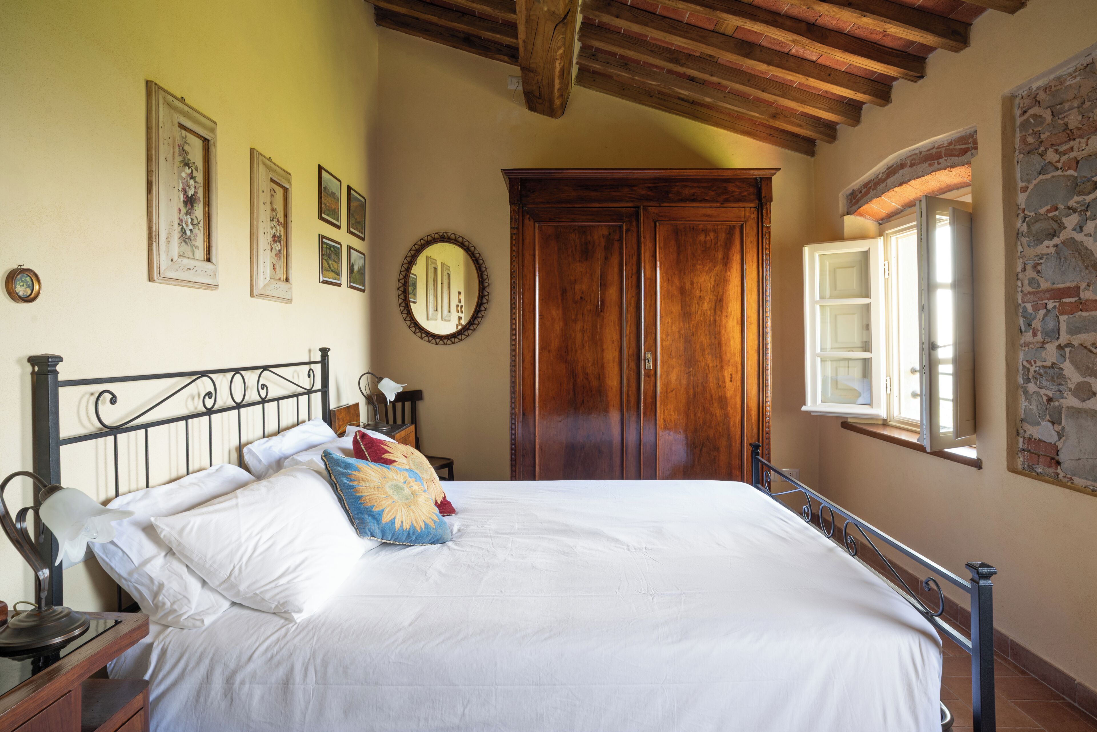 Een slaapkamer met een bed, nachtkastje, spiegel en een houten garderobe.
