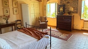 Une chambre à coucher avec un lit, une chaise, une commode et un mur en pierre.