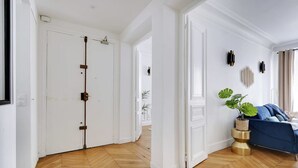 A room with a herringbone wooden floor, white walls, a blue sofa, and a plant. - Luxury 4BR Apartment - Arc de Triomphe (Paris)