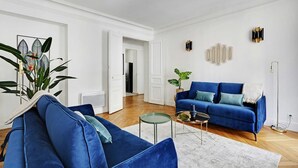A living room with a blue sofa, a small round table, and a potted plant. - Luxury 4BR Apartment - Arc de Triomphe (Paris)