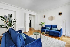 Ein Wohnzimmer mit blauem Sofa, einem kleinen runden Tisch und einem Blumentopf.