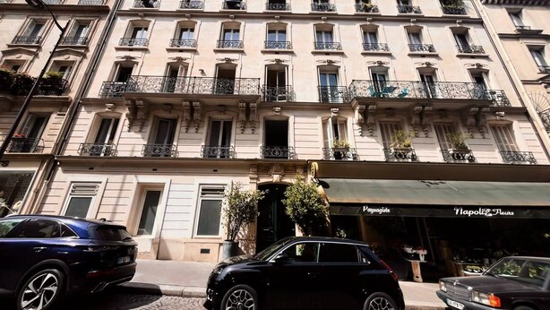 A multi-story building with balconies, a storefront with signage, and parked cars. - Luxury 4BR Apartment - Arc de Triomphe (Paris)