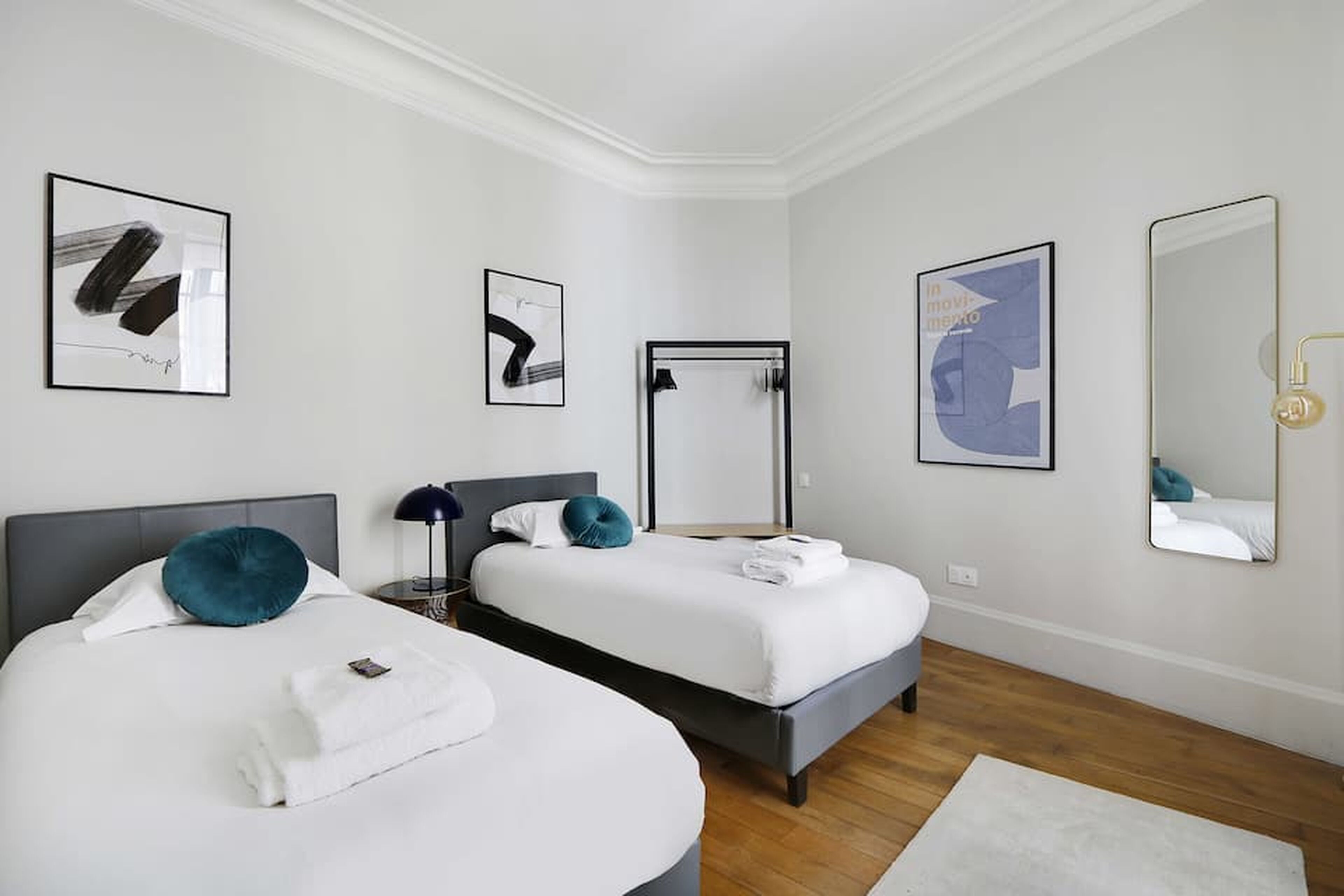 Een hotelkamer met twee bedden, een spiegel en kunstwerken aan de muur.
