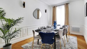 A dining area with a round table, chairs, and a potted plant. - Luxury 4BR Apartment - Arc de Triomphe (Paris)