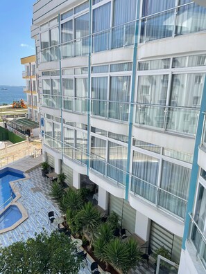 A multi-story hotel with a pool area, outdoor seating, and a view of the sea.