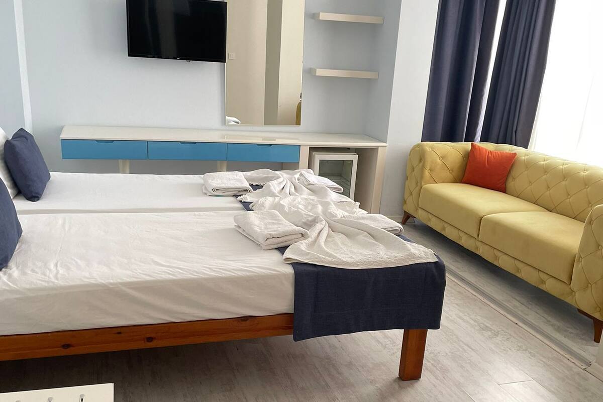 A hotel room with a bed, a TV mounted on the wall, a sofa, and a desk.
