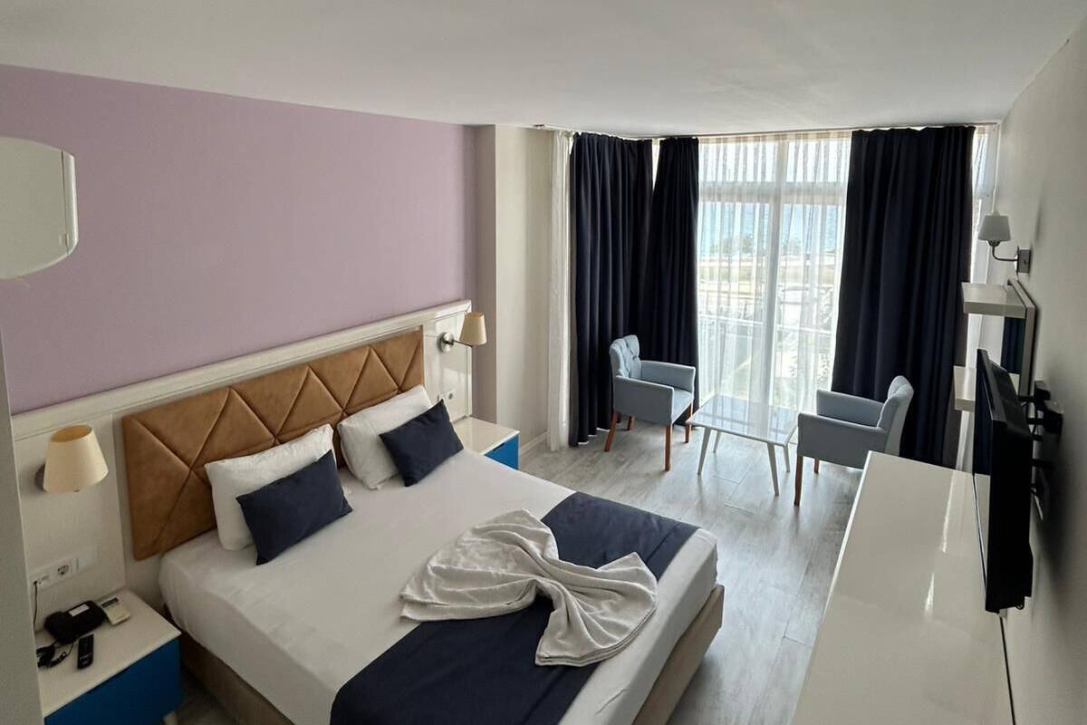 A hotel room with a bed, a desk, a chair, a TV, and a window with curtains.
