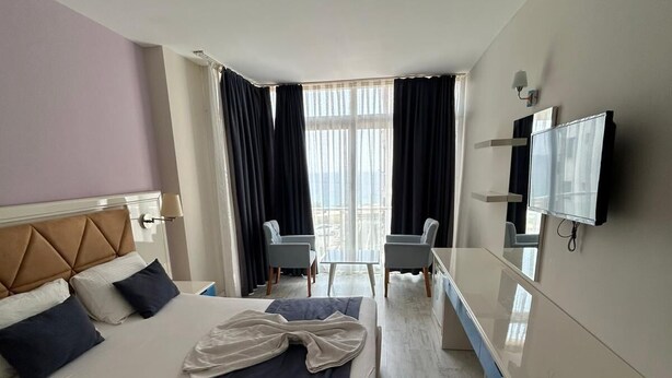 Ein Hotelzimmer mit Bett, Schreibtisch, Stuhl, Fernseher und einem Balkon mit Vorhängen.