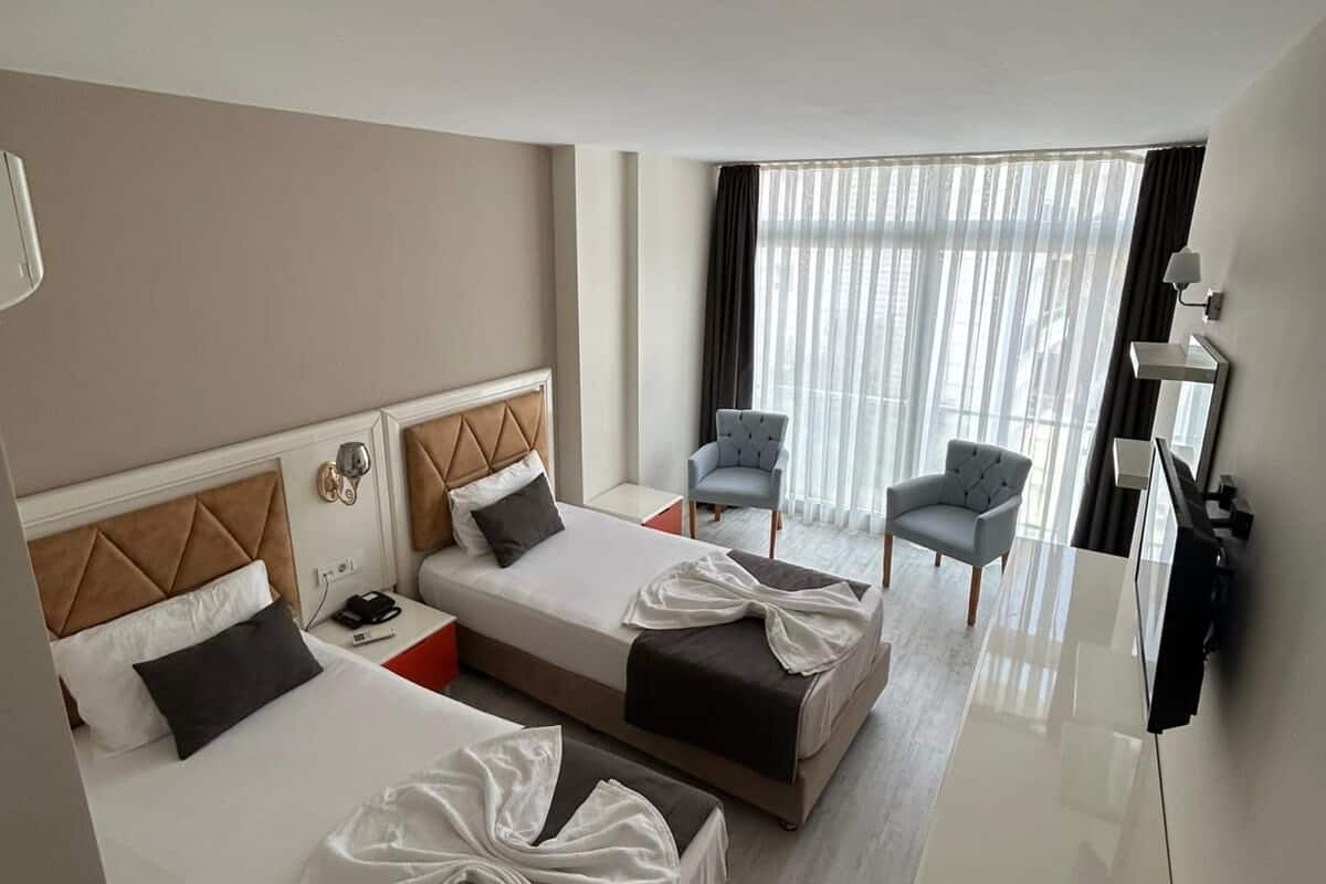 A hotel room with two beds, a desk, a chair, and a TV.
