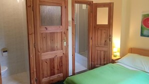 A hotel room with wooden doors, a bed with a green bedspread, a nightstand with a lamp, and a painting on the wall. - U Zeleného stromu (Janov)