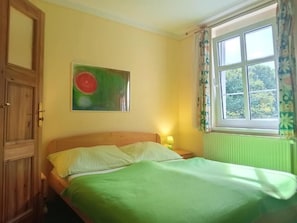 A room with a bed, a window with curtains, a radiator, and a door.