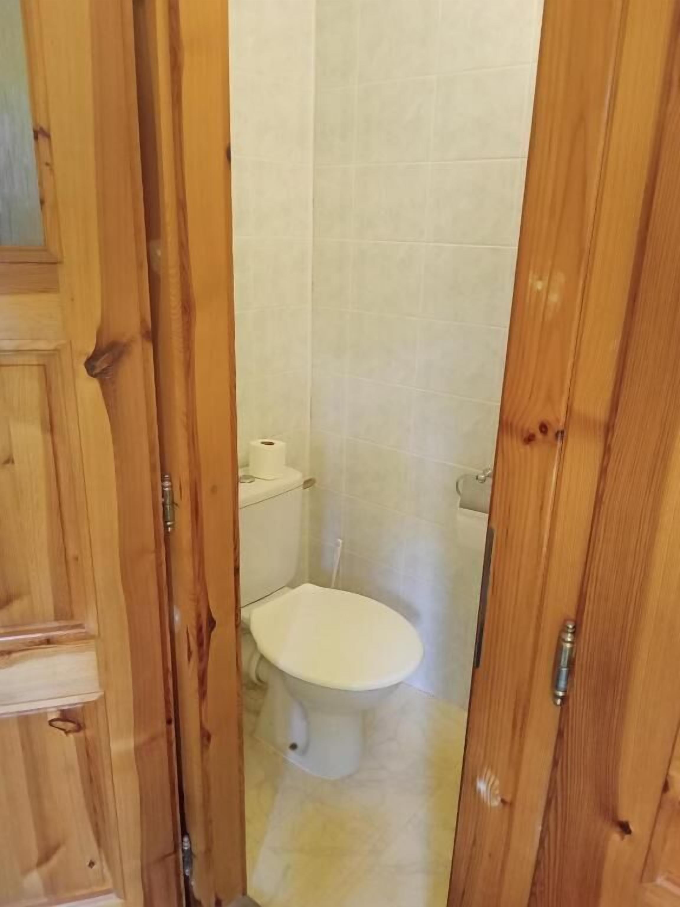 A wooden door leading to a small, tiled bathroom with a toilet and a roll of toilet paper.