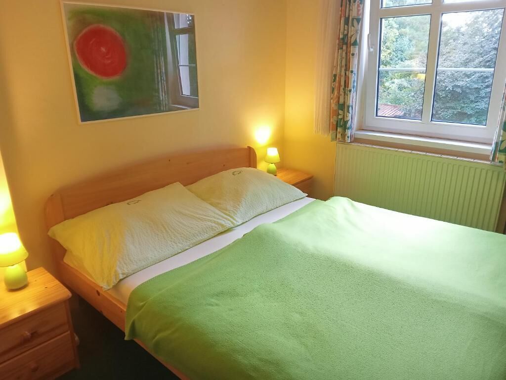 Une chambre à coucher avec un lit, deux lampes de chevet, une fen être avec des rideaux et un tableau au mur.