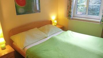 Een slaapkamer met een bed, twee bedlampen, een raam met gordijnen en een schilderij aan de muur.