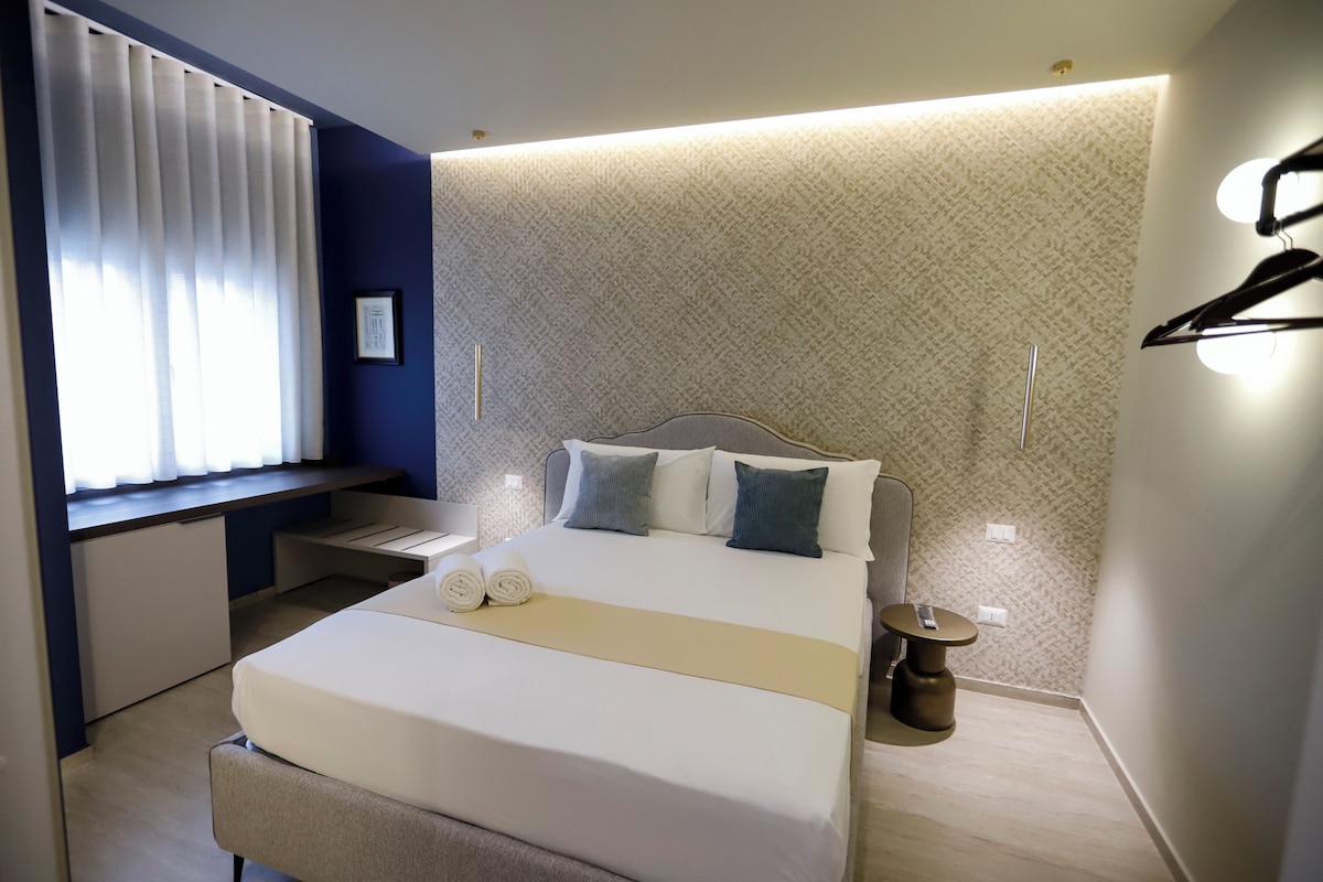 Una habitación de hotel moderna con cama, mesita de noche y un escritorio con silla.