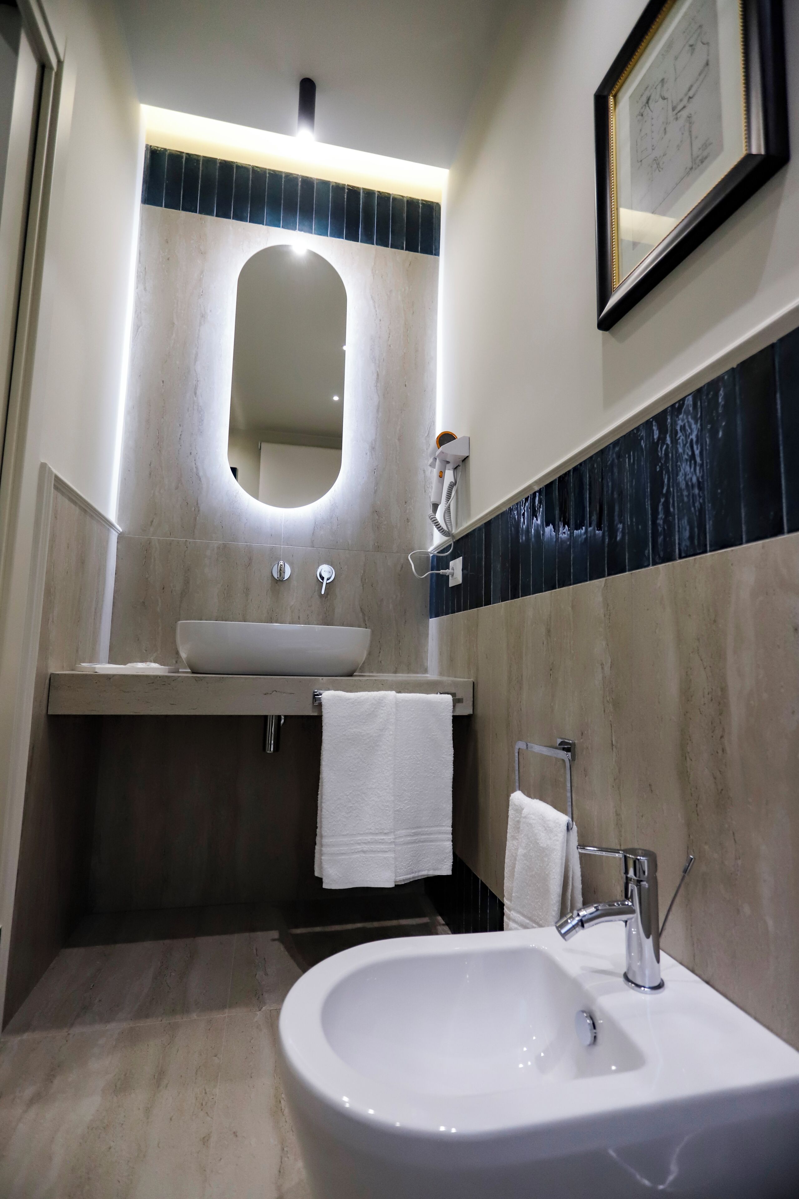 Une salle de bain équipée d’un lavabo, d’un miroir, d’un porte-serviettes et d’un tableau encadré au mur.