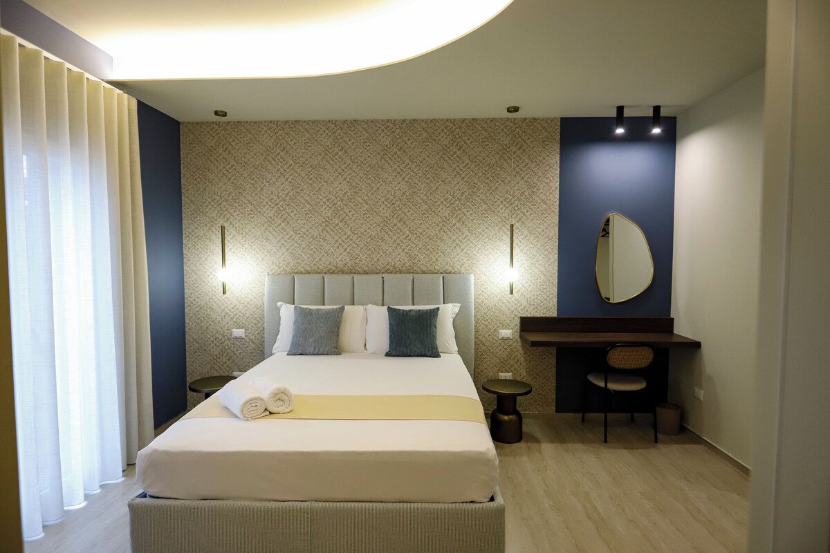 Una habitación de hotel con cama, mesitas de noche, escritorio, silla y espejo.
